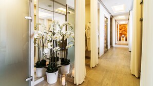 Un couloir d’hôtel avec un plancher en bois, des rideaux blancs et des orchidées blanches en pot.