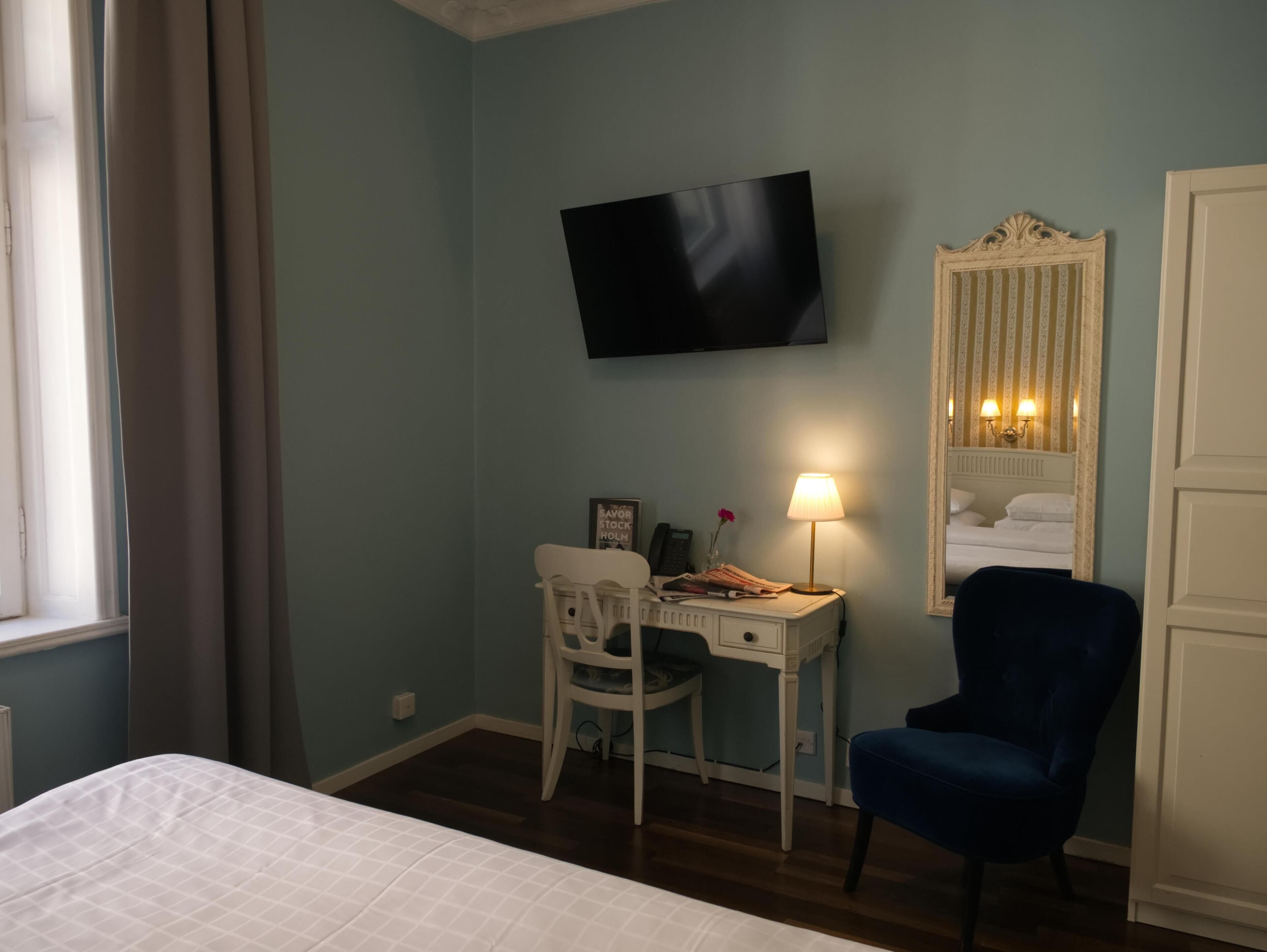 Een hotelkamer met een bed, een bureau met stoel, een aan de muur bevestigde televisie, een nachtkastje met lamp en een spiegel met verlichting.