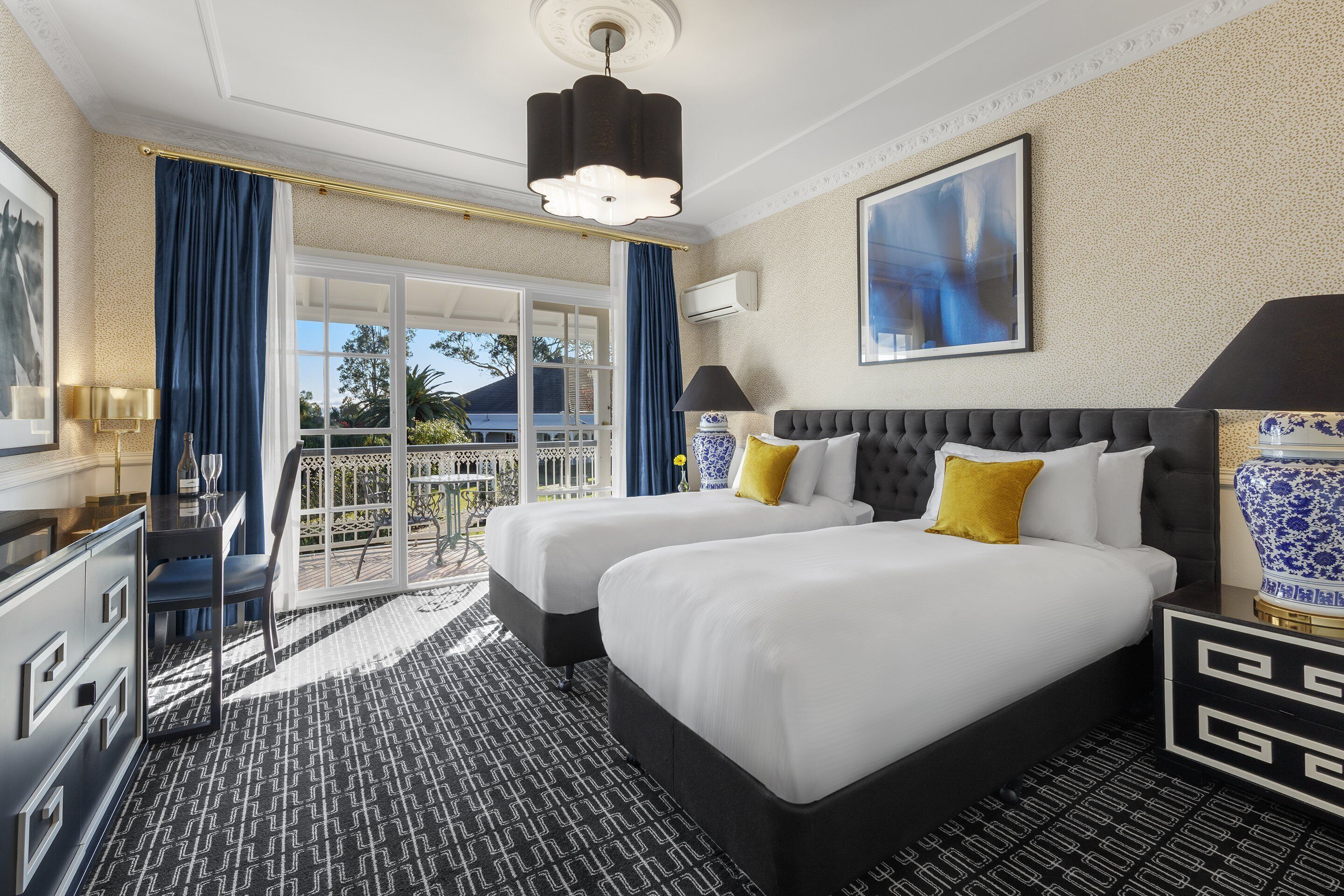 A hotel room with two beds, a balcony, a desk, and a large window.