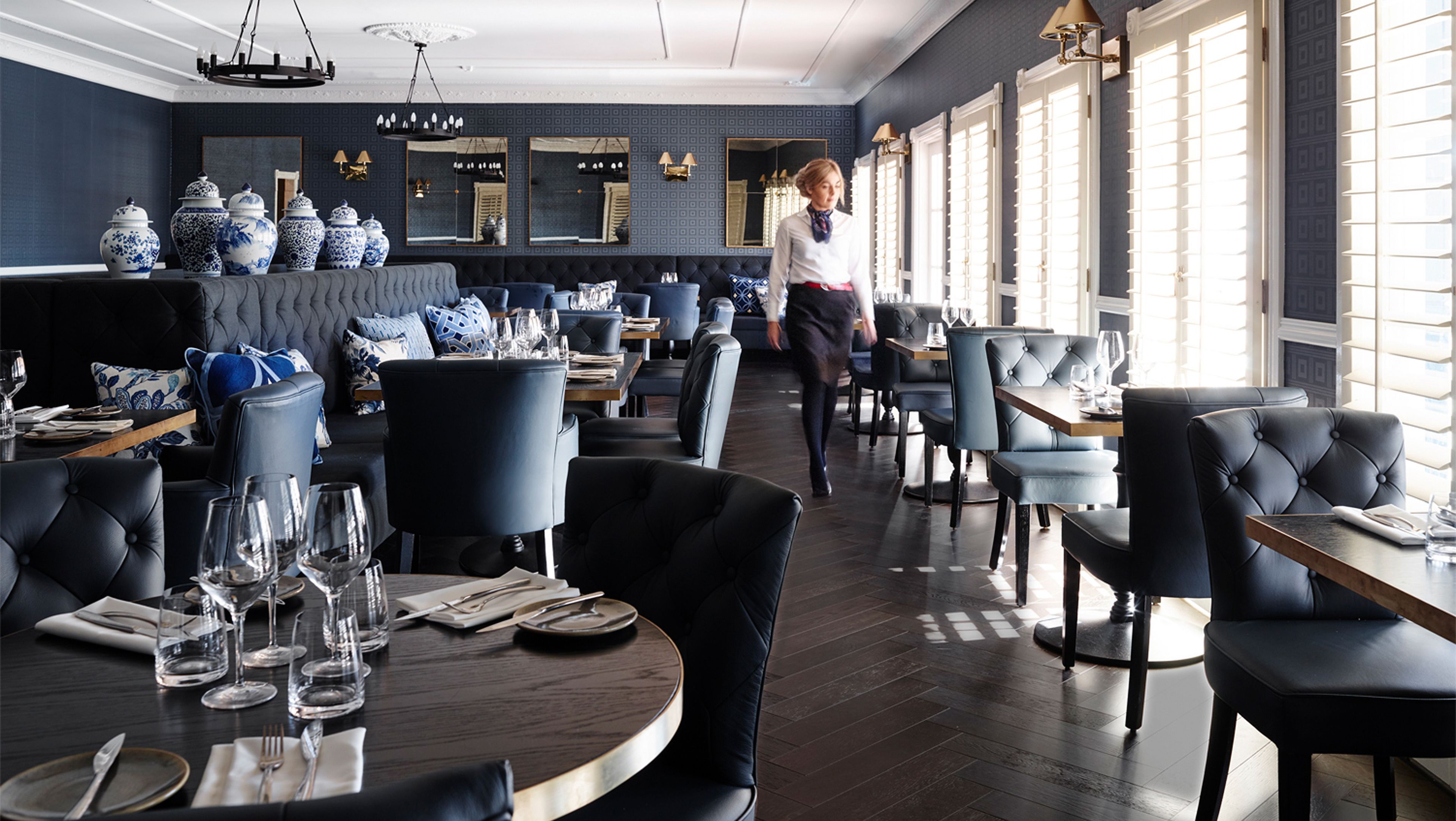 Ein Restaurant mit runden Tischen, blau gepolsterten Stühlen und einem Kellner, der durch den Raum geht.