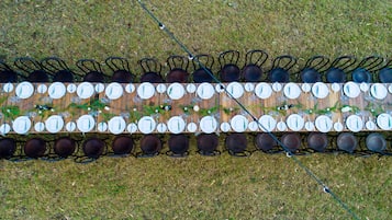 A long dining table set with multiple chairs, plates, and cutlery, arranged outdoors on grass.