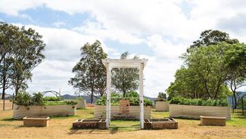 A garden with a white pergola structure surrounded by raised garden beds and trees.