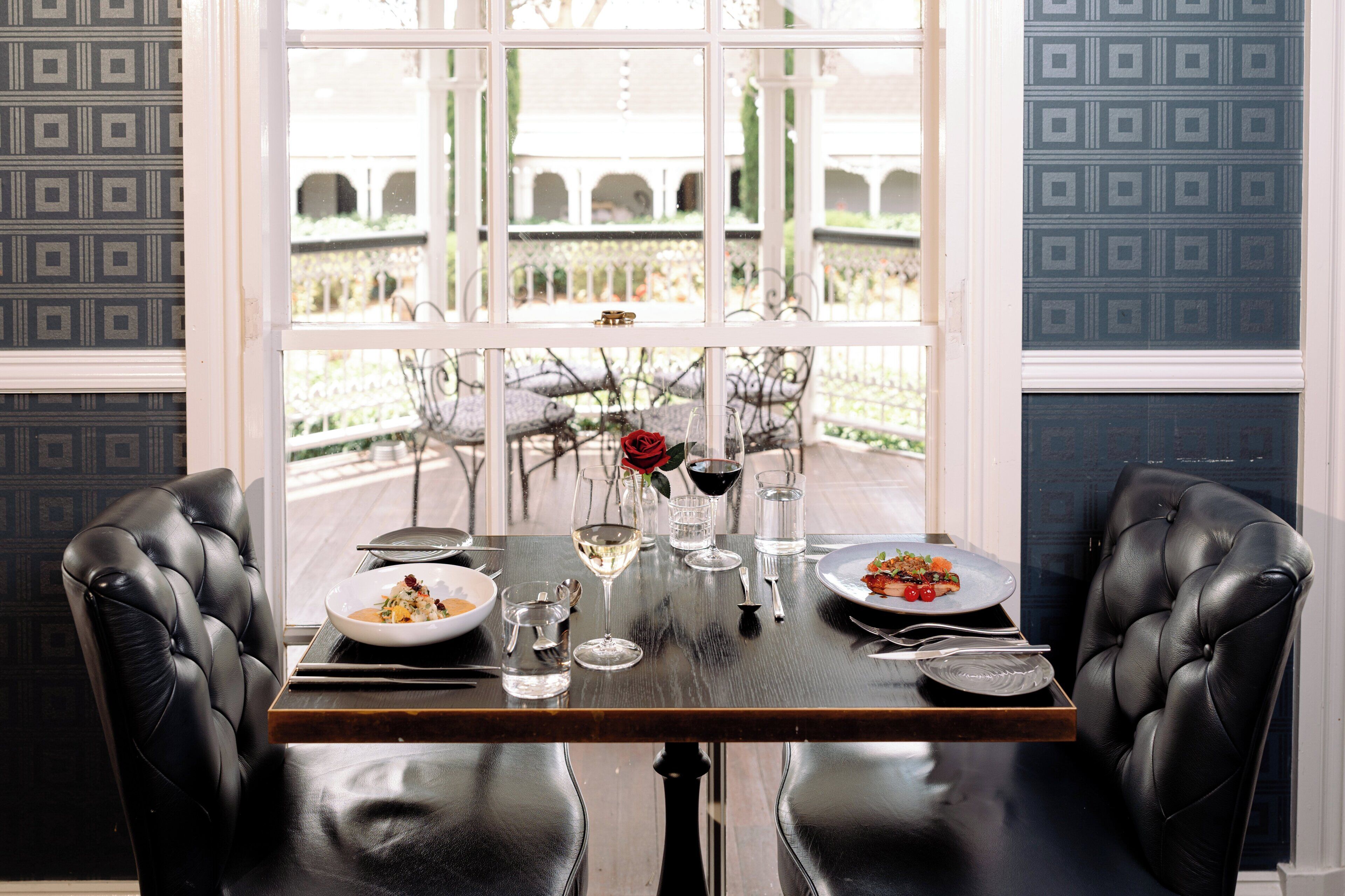 A dining table set for two with plates of food, wine glasses, and cutlery.