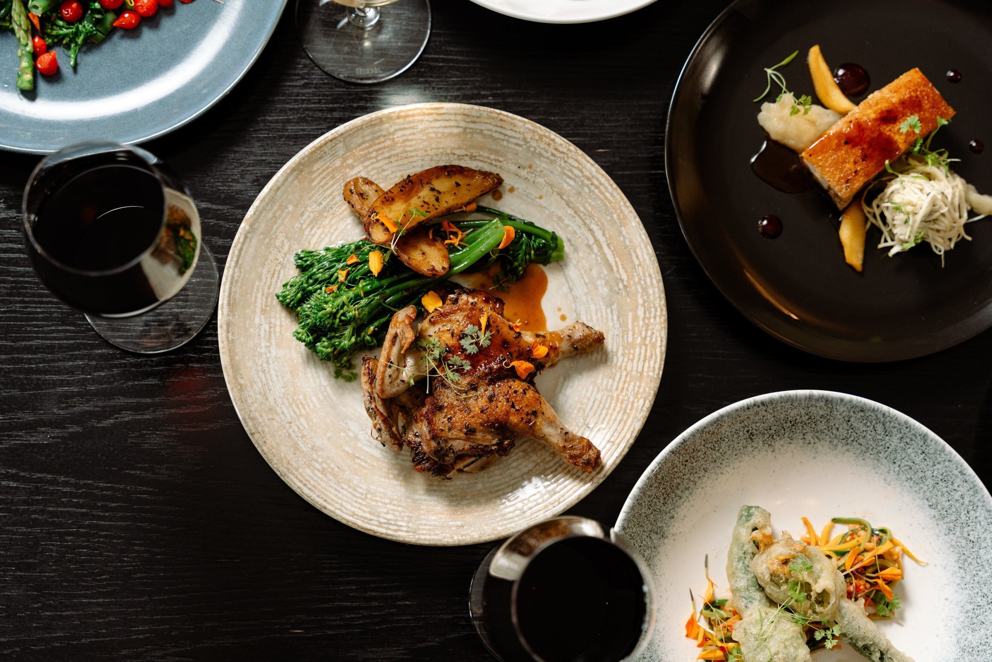 A dining table with multiple plates of food, including roasted chicken, vegetables, and a dessert.