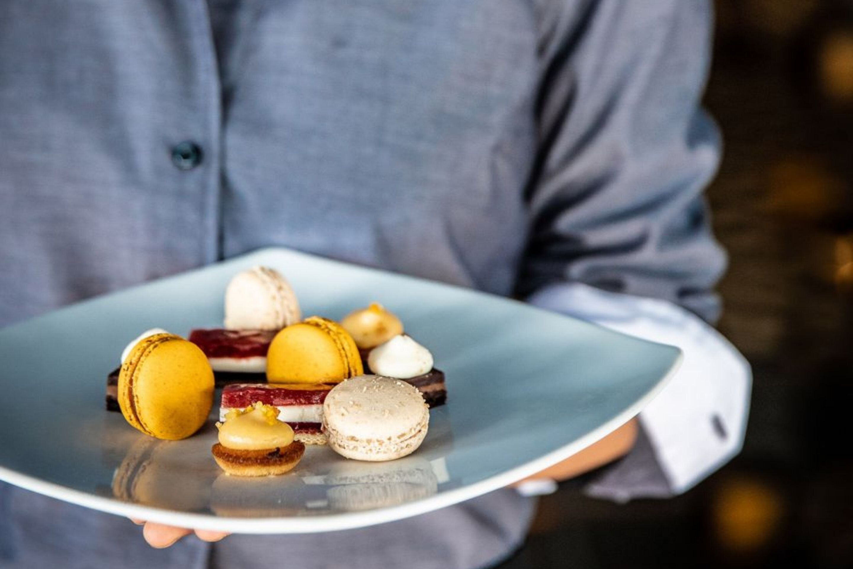 A person holding a plate with macarons and other desserts.