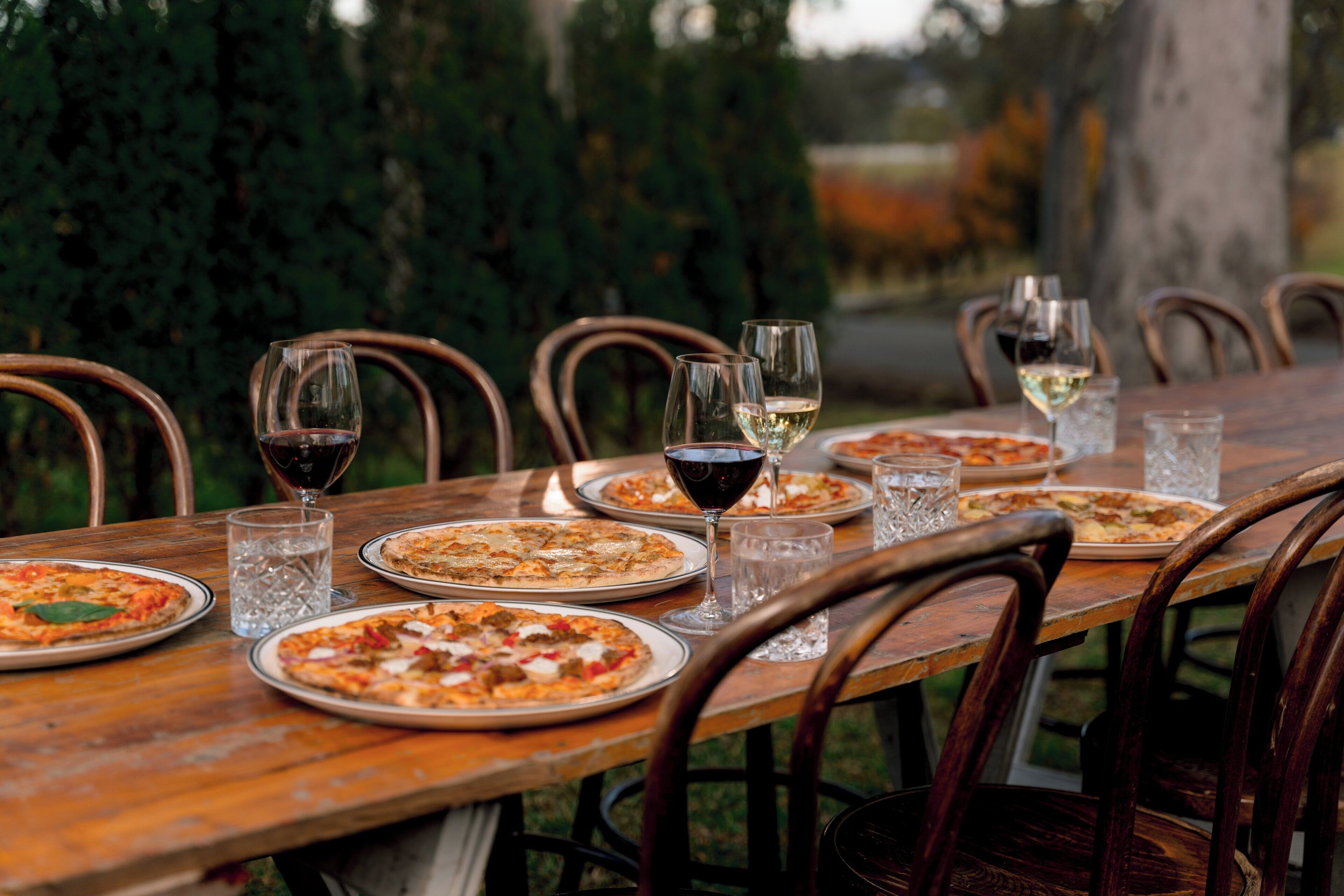 A wooden dining table with plates of pizza and glasses of wine, surrounded by chairs.