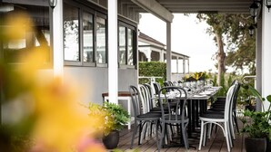 An outdoor dining area with a covered patio, tables set with chairs, and potted plants.