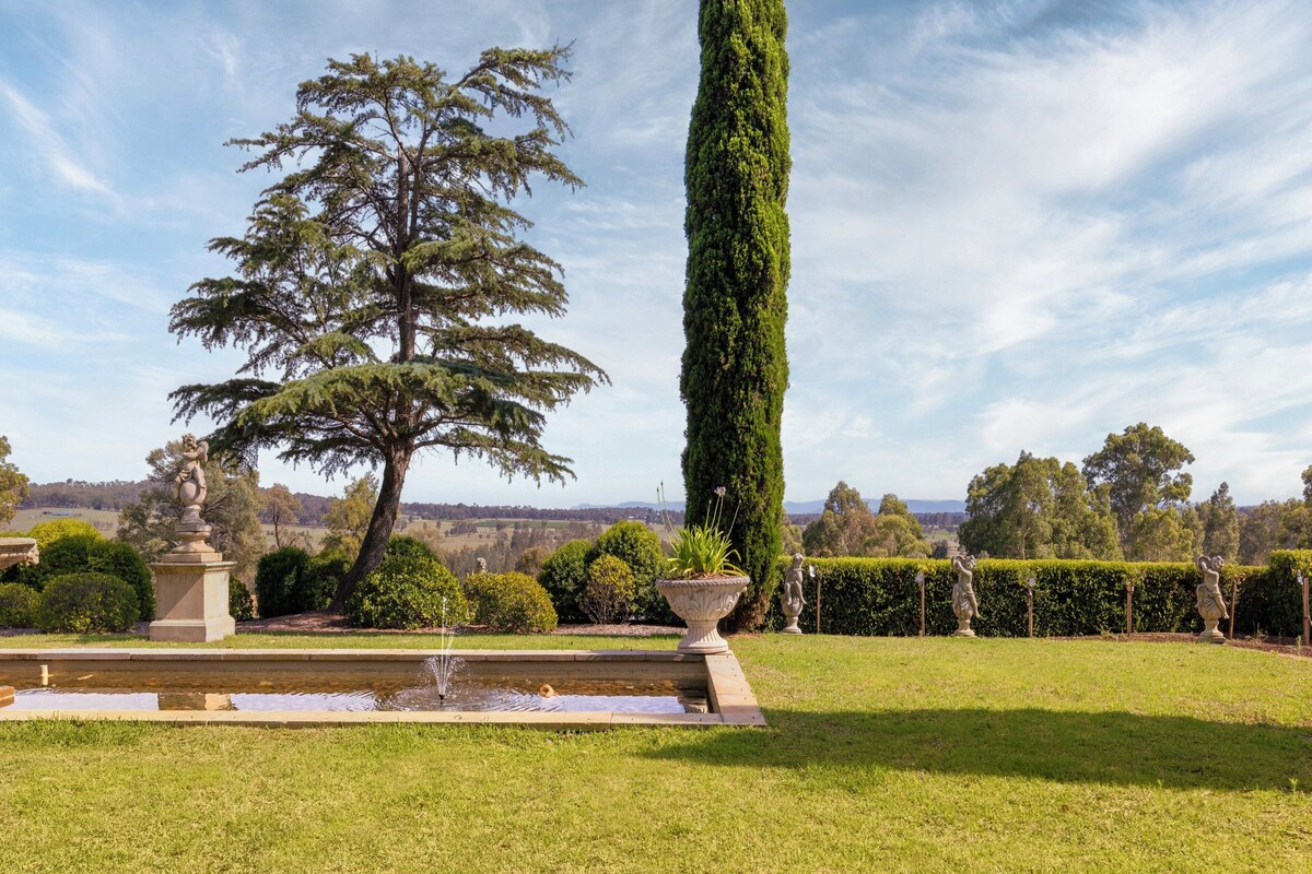 A well-maintained garden with a fountain, statues, and a tall tree.