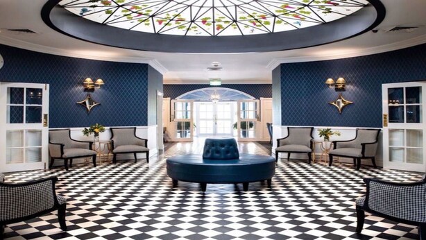 A lobby with a checkered floor, a central seating area, and a ceiling with a stained glass design.