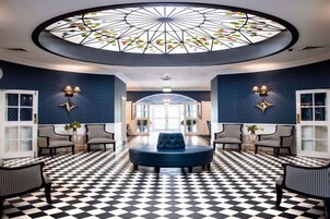 Un hall con piso a cuadros, un área de estar central y un techo con diseño de vitral.