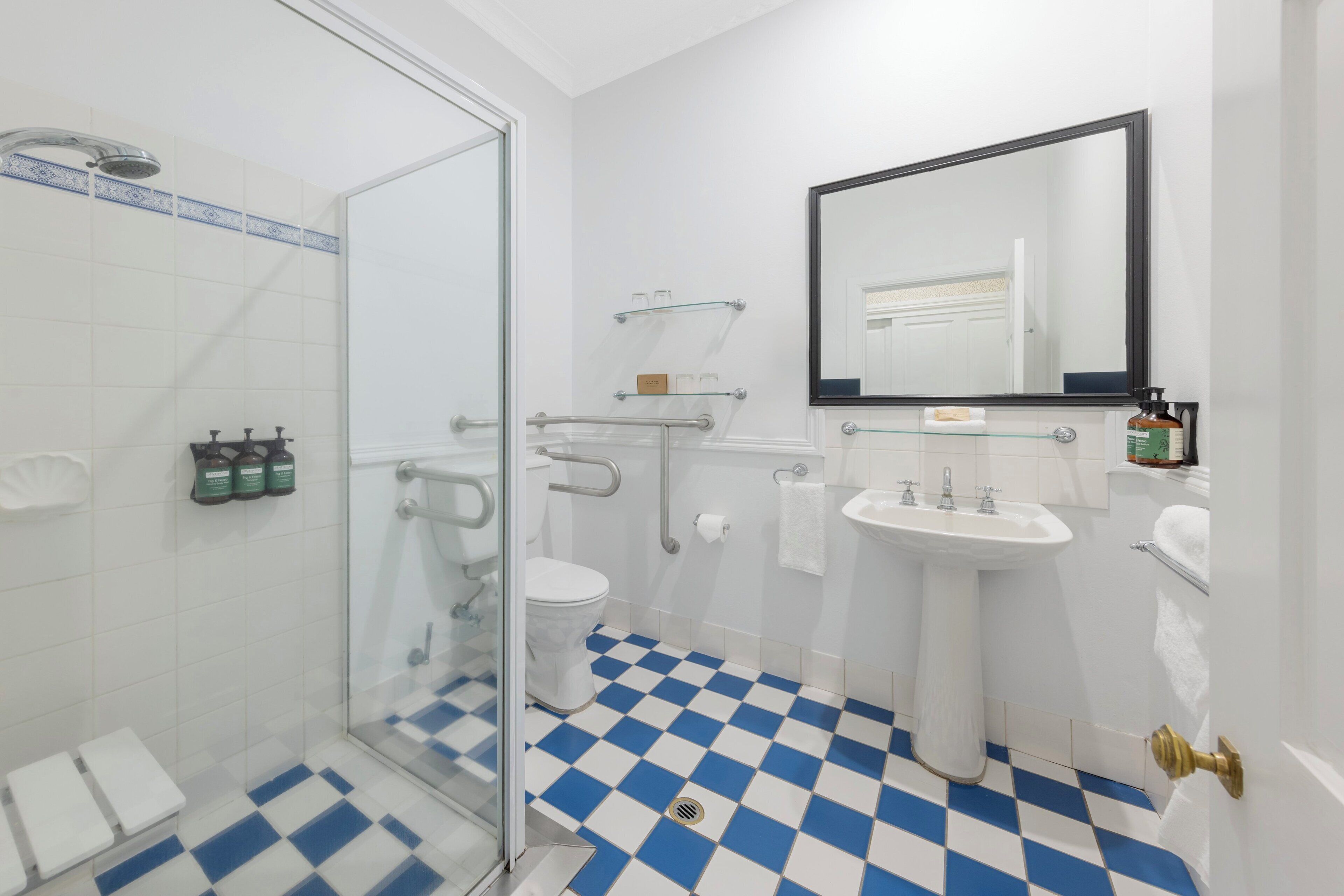 A bathroom with a glass shower enclosure, a white sink, and a checkered floor.