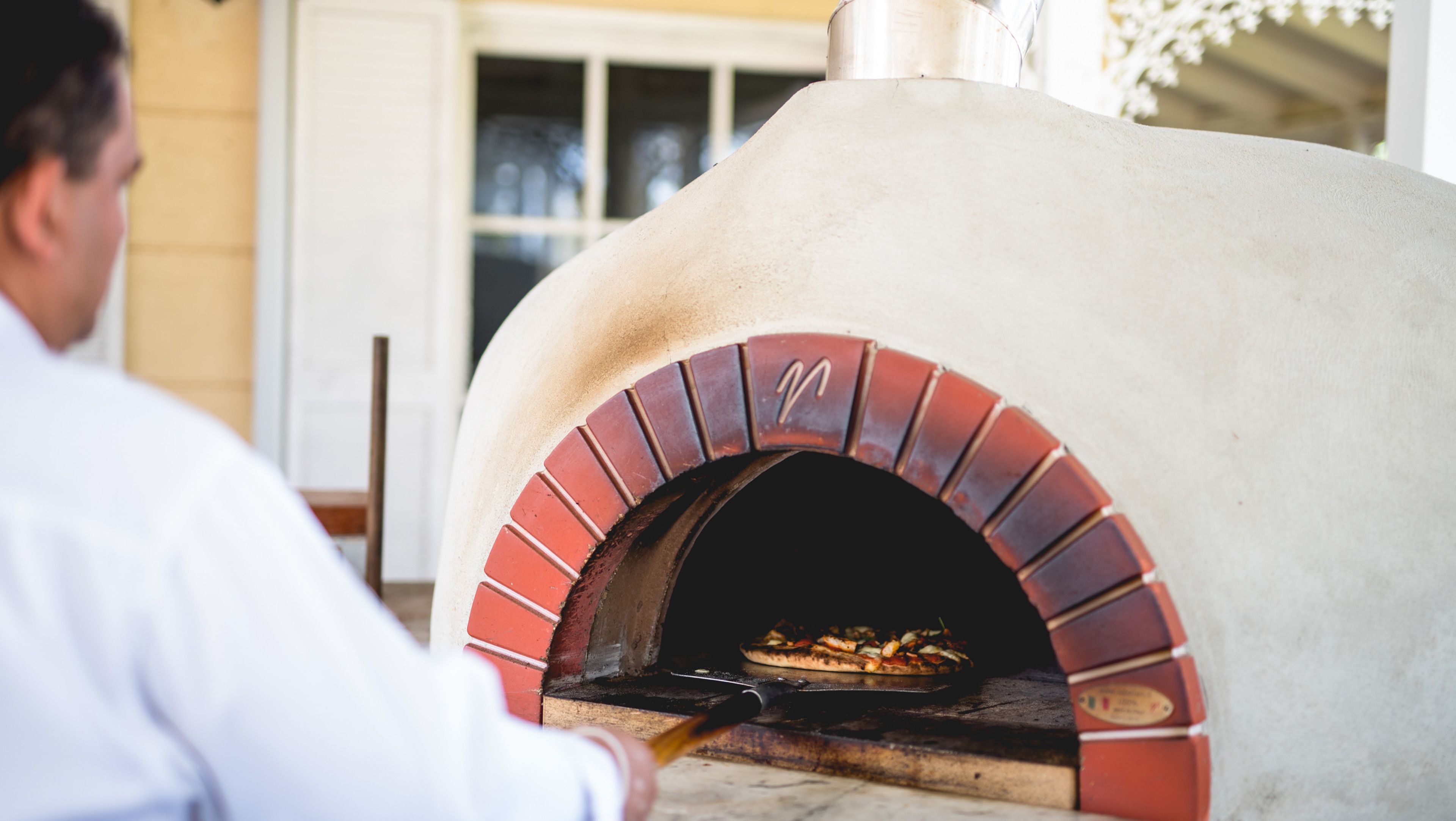 A person using a pizza oven with a brick interior and a chimney.