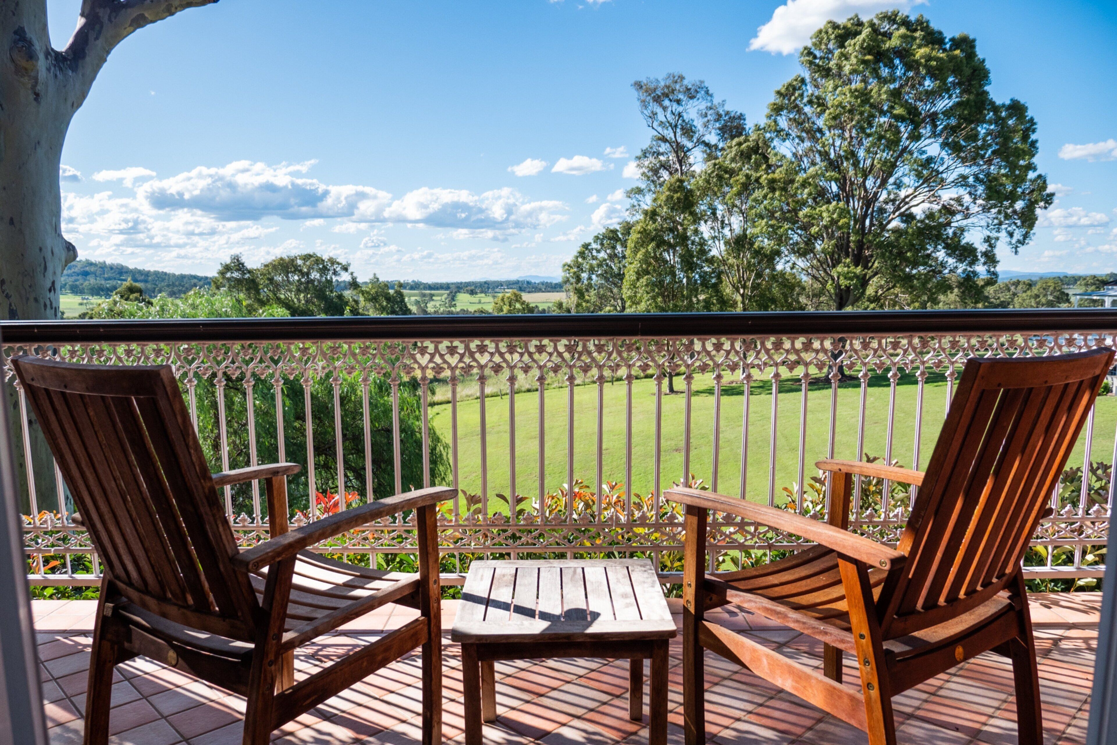 A wooden deck with two chairs and a table, overlooking a green field and trees.
