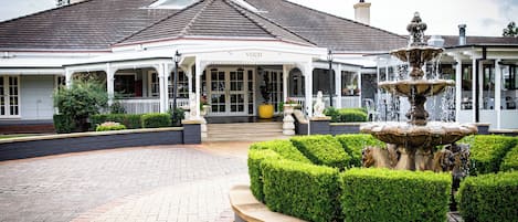A building with a covered entrance, a fountain, and a well-maintained garden.