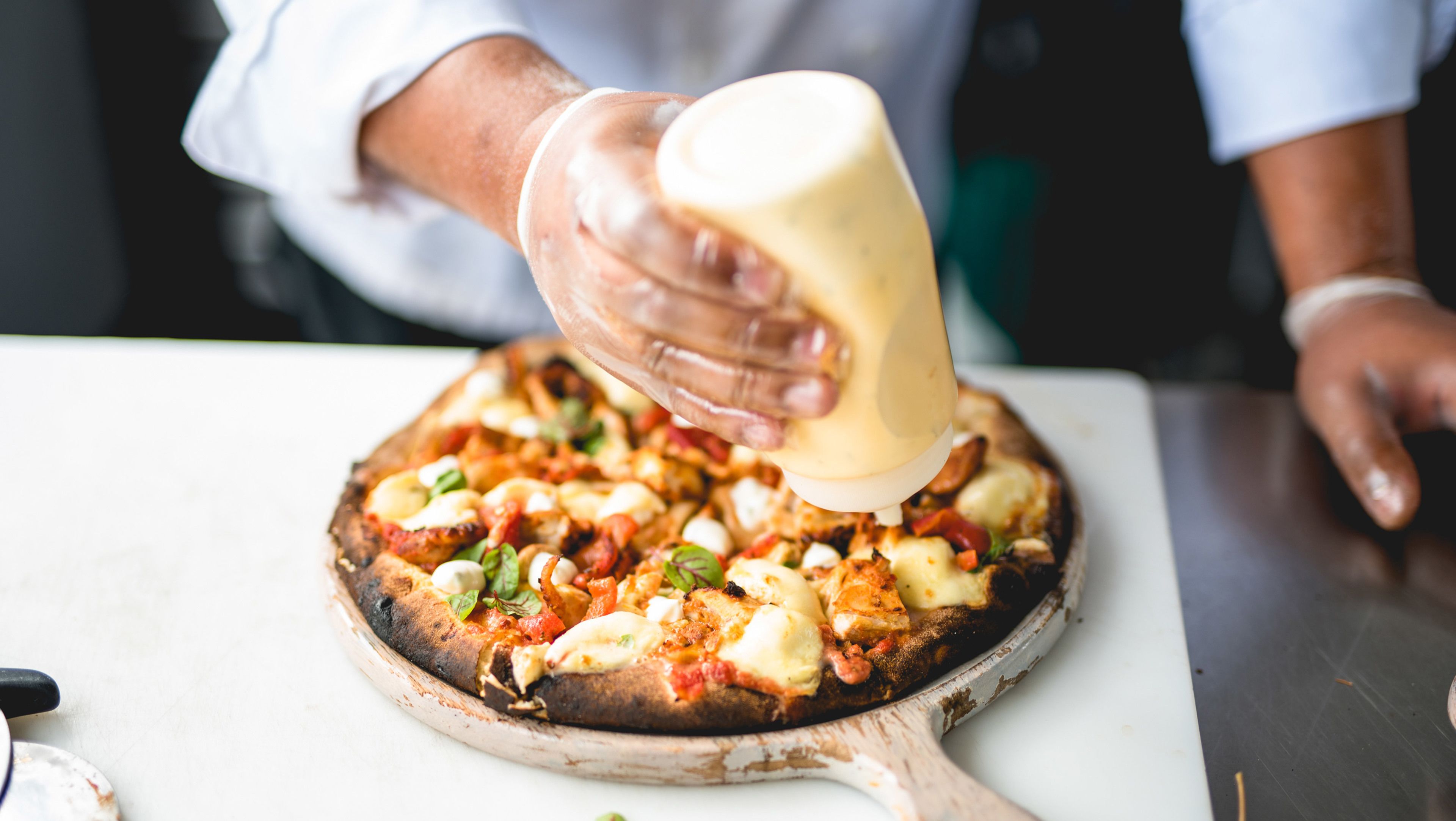 A person pouring sauce onto a pizza on a wooden board.
