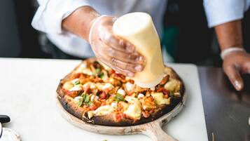 Alguém despejando molho em uma pizza sobre uma tábua de madeira.