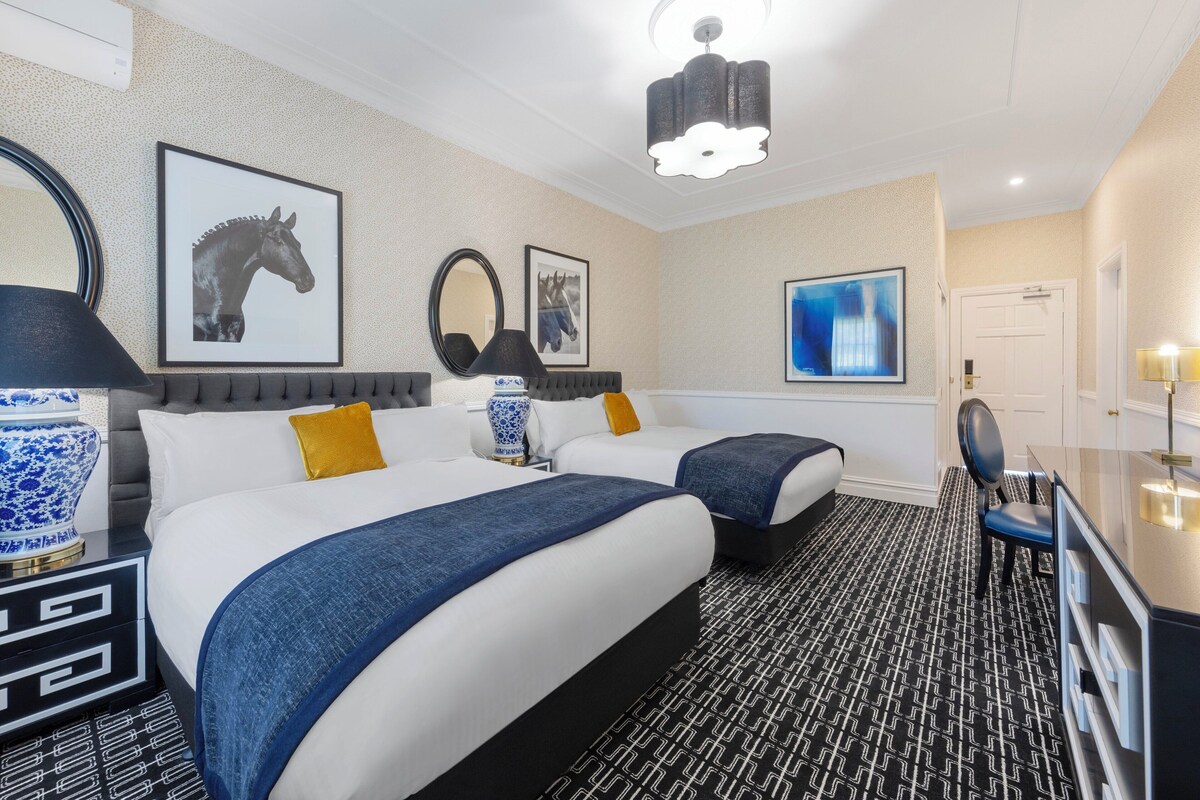 A hotel room with two beds, a desk, a chair, and a large mirror.