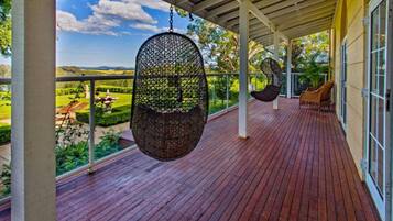 Um deck de madeira com cadeiras e balanço pendurados, com vista para um jardim paisagístico.