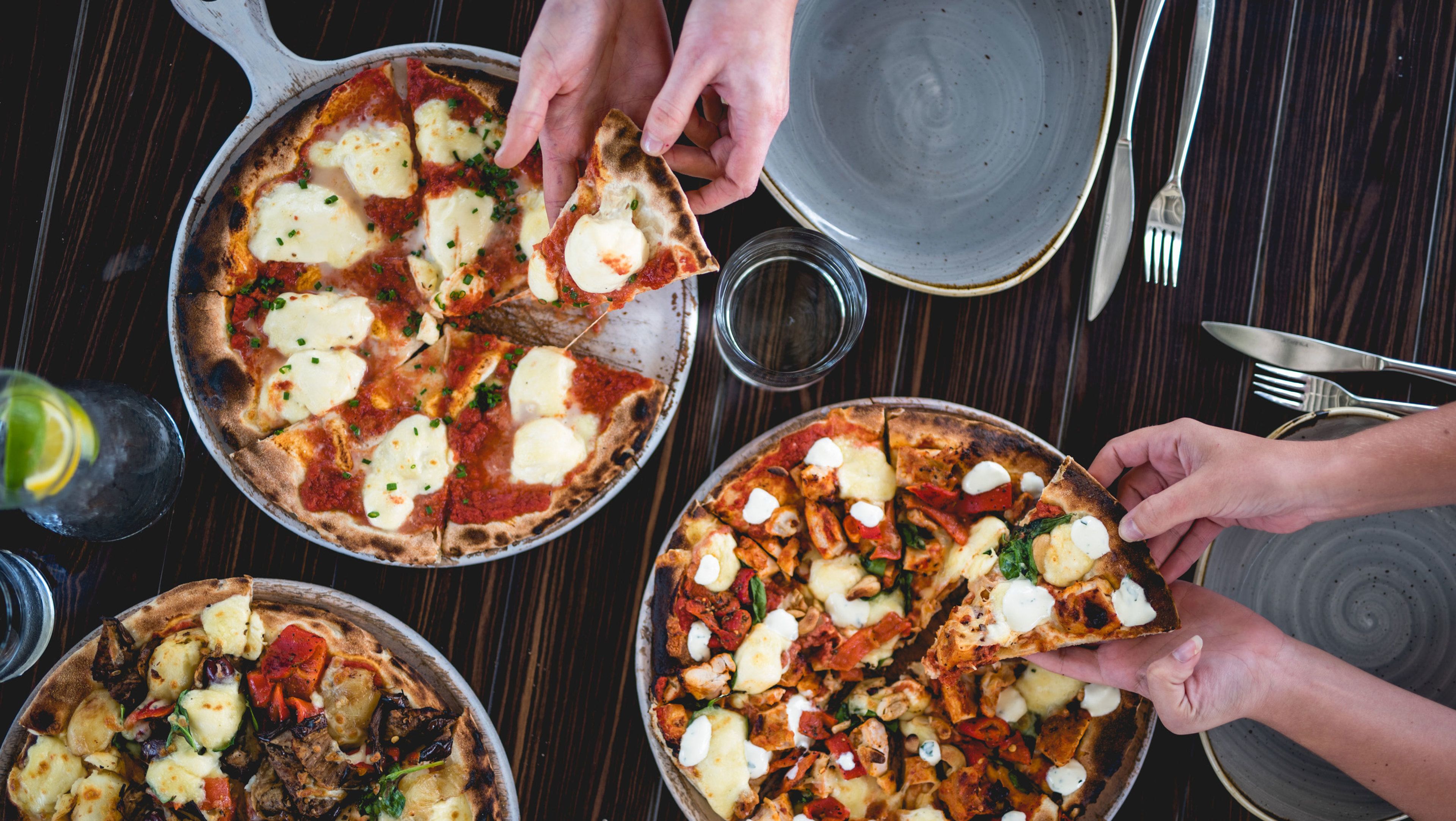 Three pizzas on a table with utensils and a glass of water nearby.