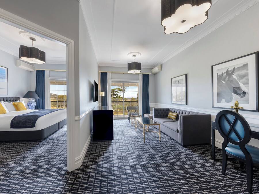 Una habitación de hotel con cama, sofá, sillón, escritorio y un ventanal grande.