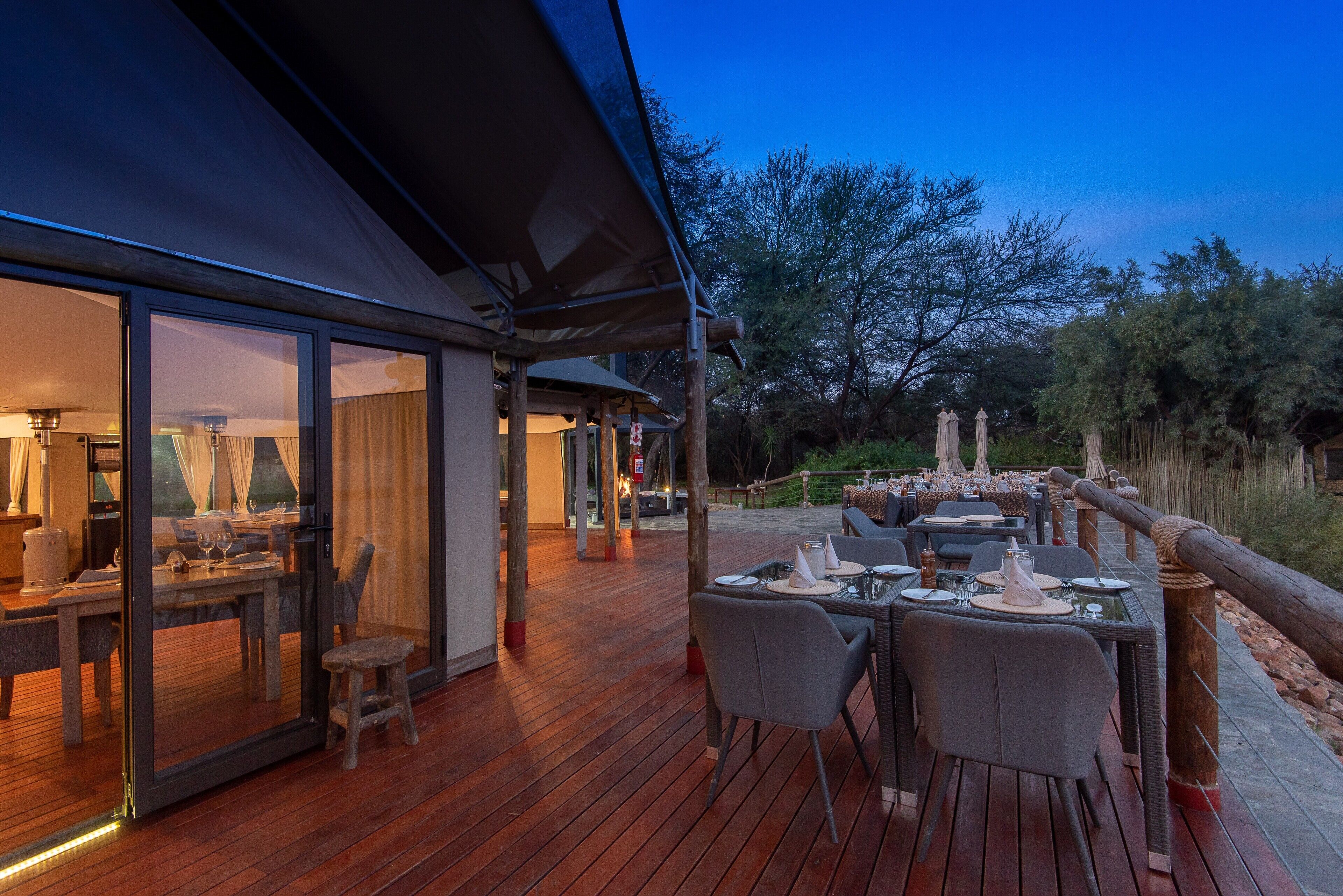 An outdoor dining area with tables and chairs, a wooden deck, and a view of the surrounding landscape.