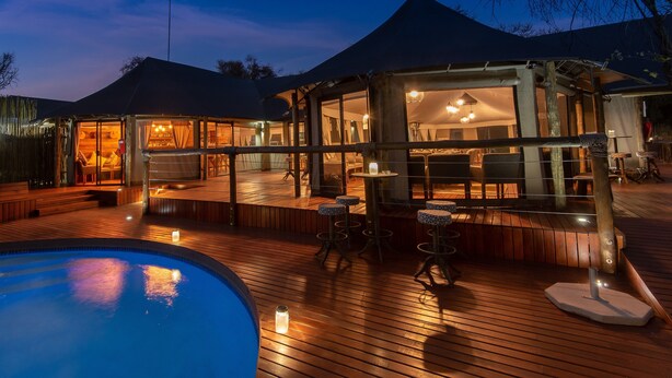 A wooden deck with a pool, outdoor seating, and a covered area with tables and chairs. - Tau Game Lodge (Ramotshere Moiloa)