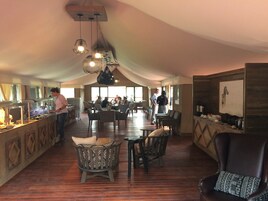 Un restaurante espacioso con techos altos, varias mesas y sillas para comer, y una zona de bar central.