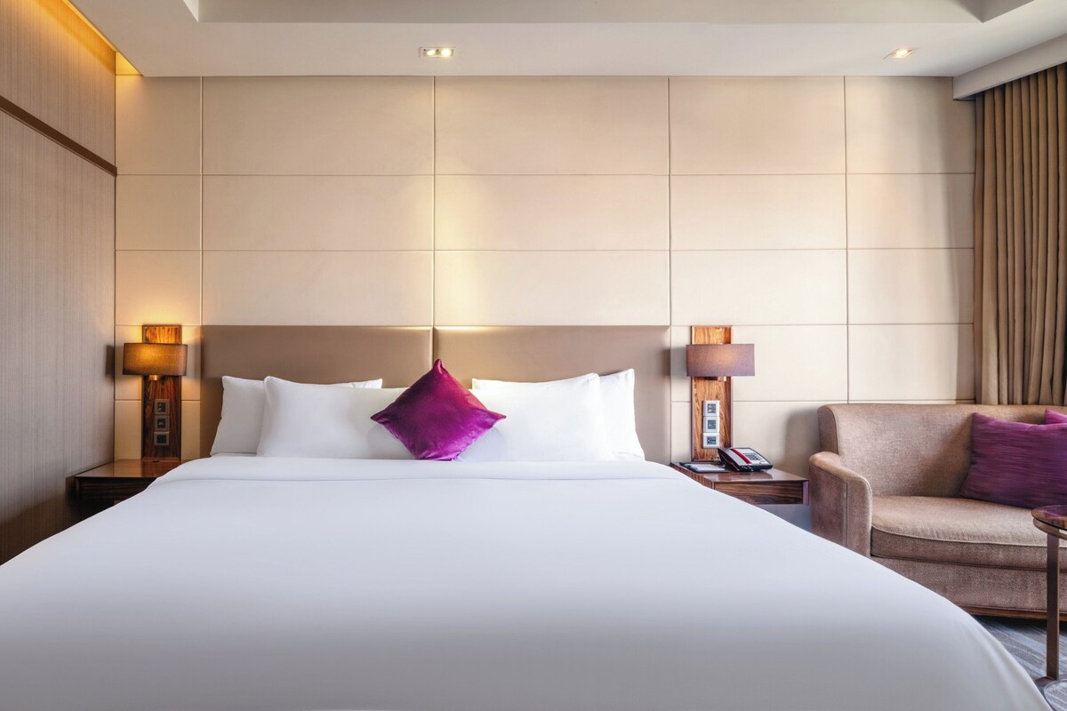 Una habitación de hotel con una cama grande, dos lámparas de noche, una silla y una mesita de noche con un teléfono.