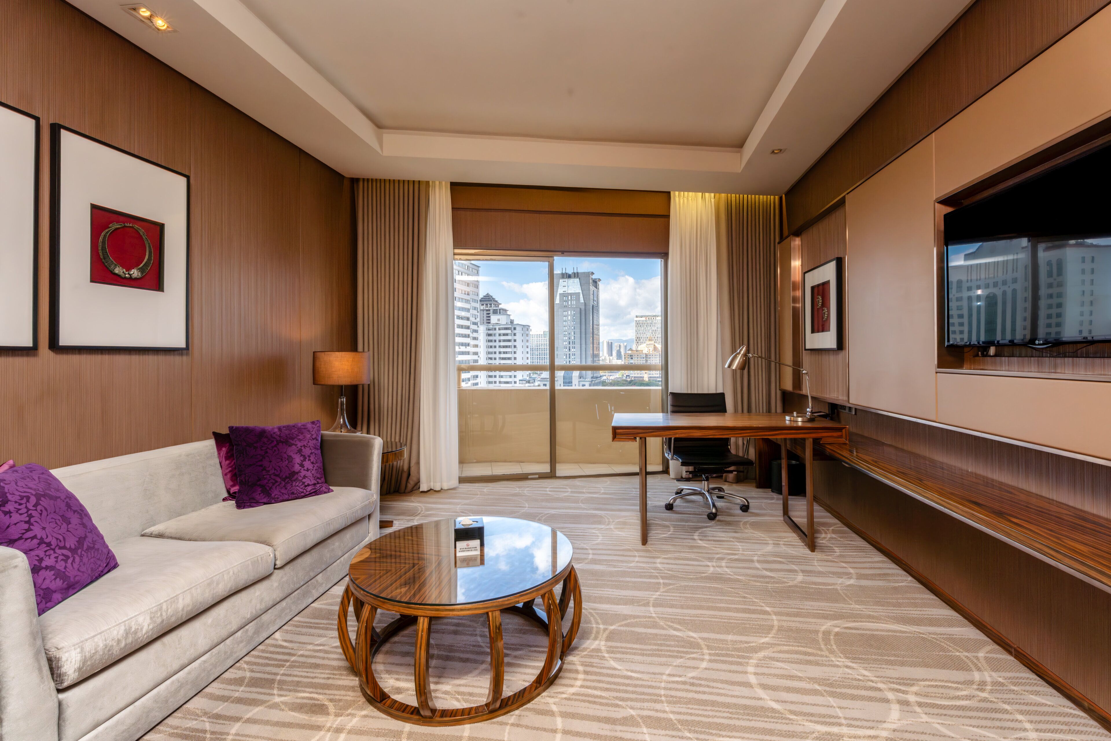 Une chambre d’hôtel avec un canapé, une table ronde, un bureau, une télévision et une vue sur la ville.