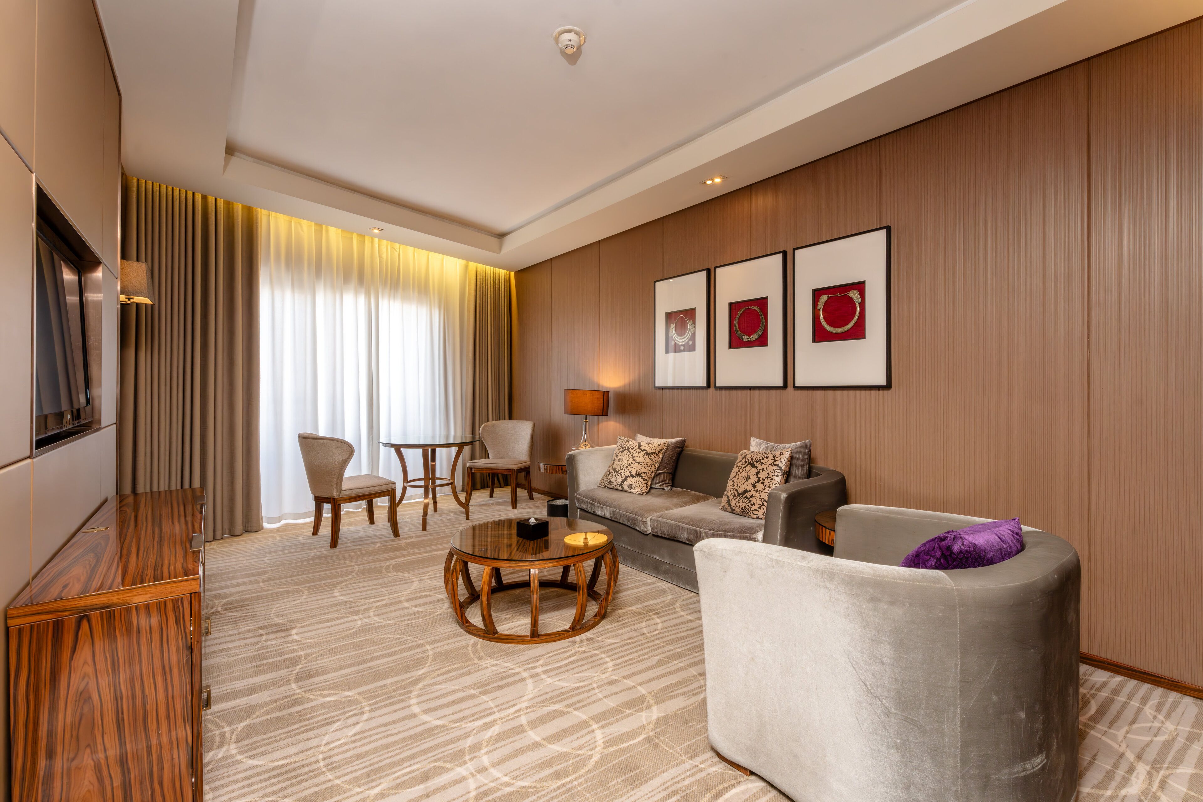 A modern hotel room with a sofa, armchair, round coffee table, and a TV.