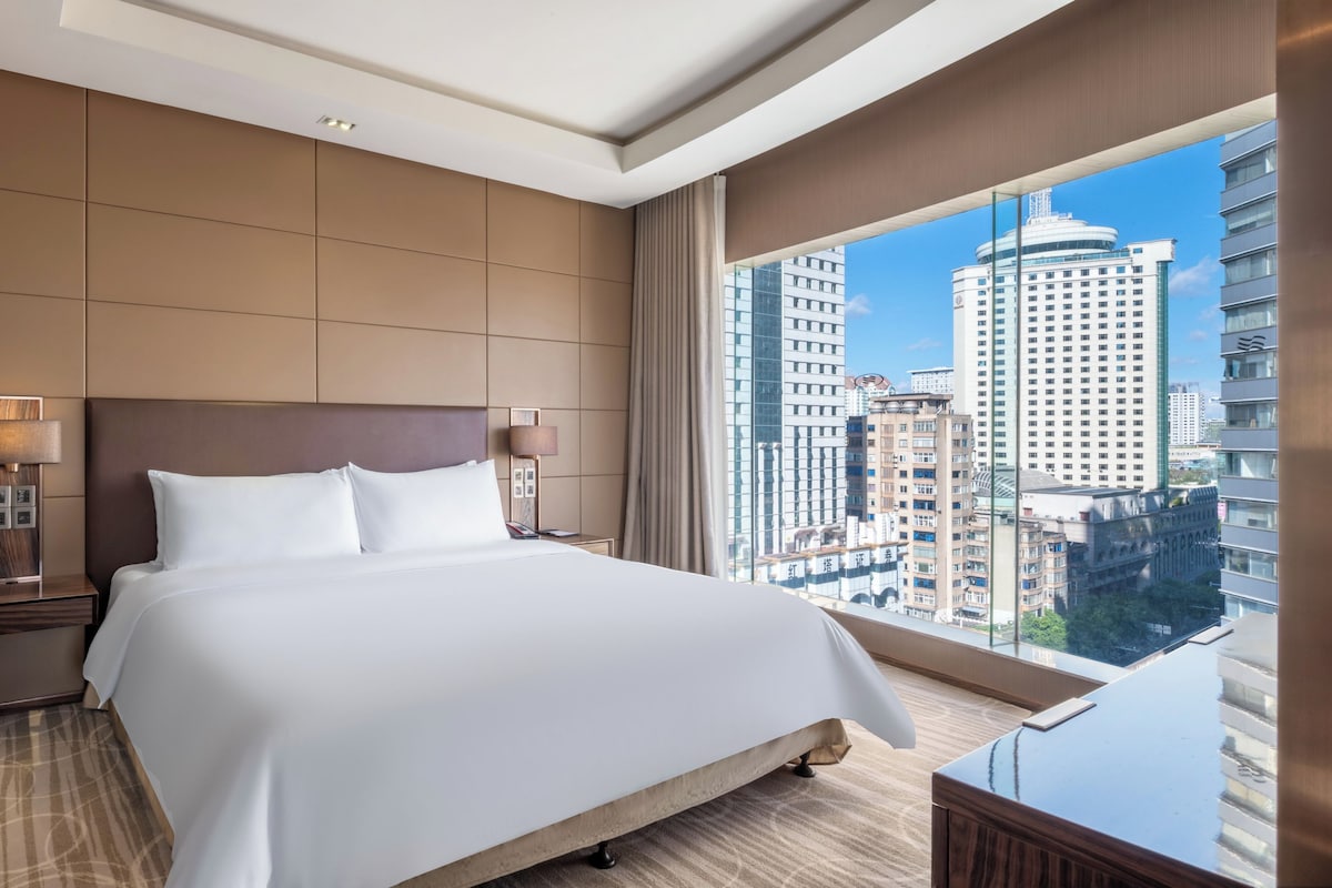 Een hotelkamer met een groot bed, een nachtkastje met lamp, uitzicht op de stad door het raam en een modern design.