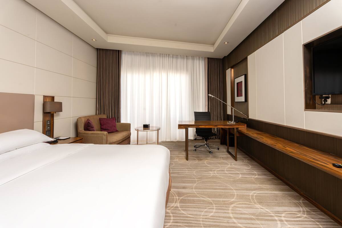Una habitación de hotel con una cama grande, un escritorio, una silla, una mesita y un televisor montado en la pared.