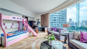 Habitación de hotel moderna con literas, escritorio, sofá y un amplio ventanal con vista a la ciudad.