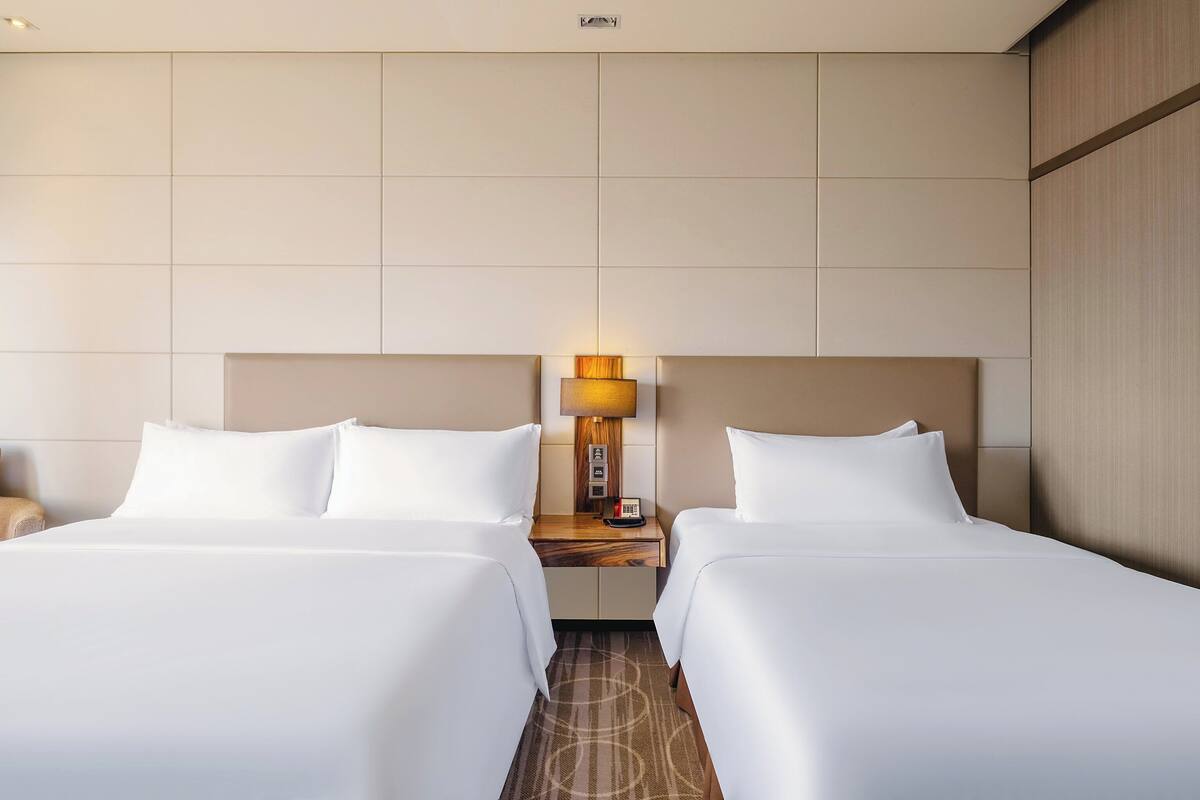 Una habitación de hotel con dos camas, una mesita de noche con lámpara y un sofá.