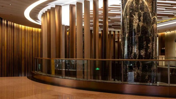 Een moderne lobby met verticale zuilen, een glazen balustrade en een grote marmeren kolom.