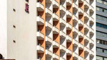 Un edificio alto con un diseño repetido de balcones y un letrero vertical llamativo.