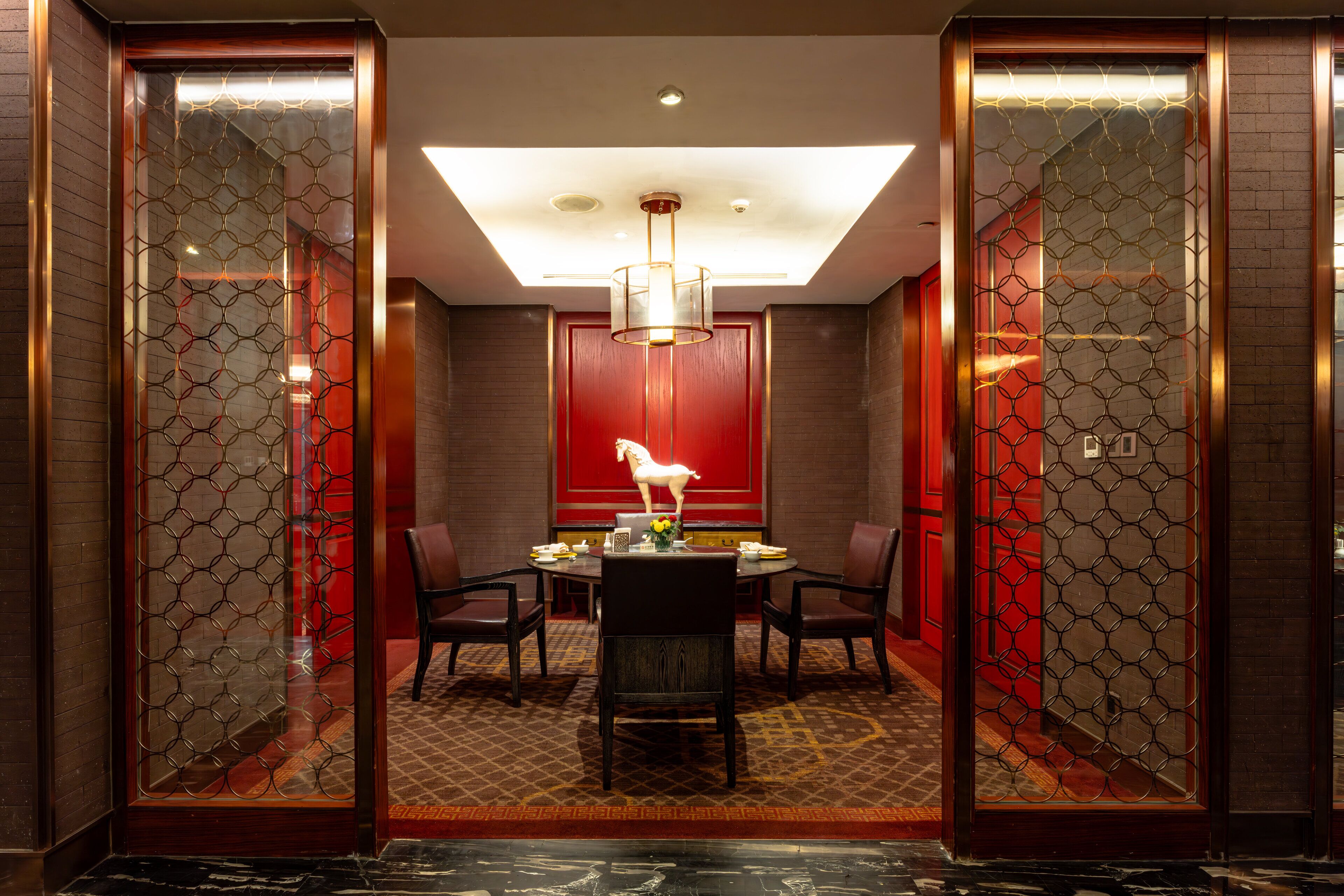 A hotel room with a dining table, chairs, a chandelier, and a red accent wall.