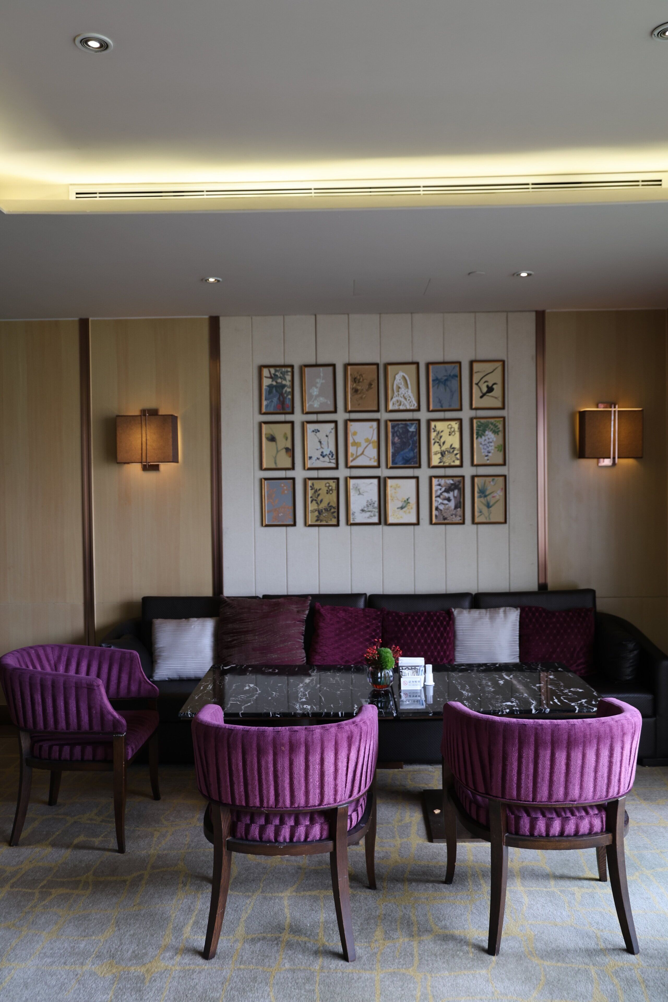 A room with a sofa, two purple chairs, a table, and wall-mounted artwork.