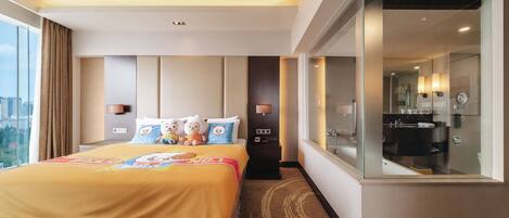 Habitación de hotel con una cama grande, vistas a la ciudad, un baño con cabina de ducha de vidrio y una mesita de noche con lámpara.