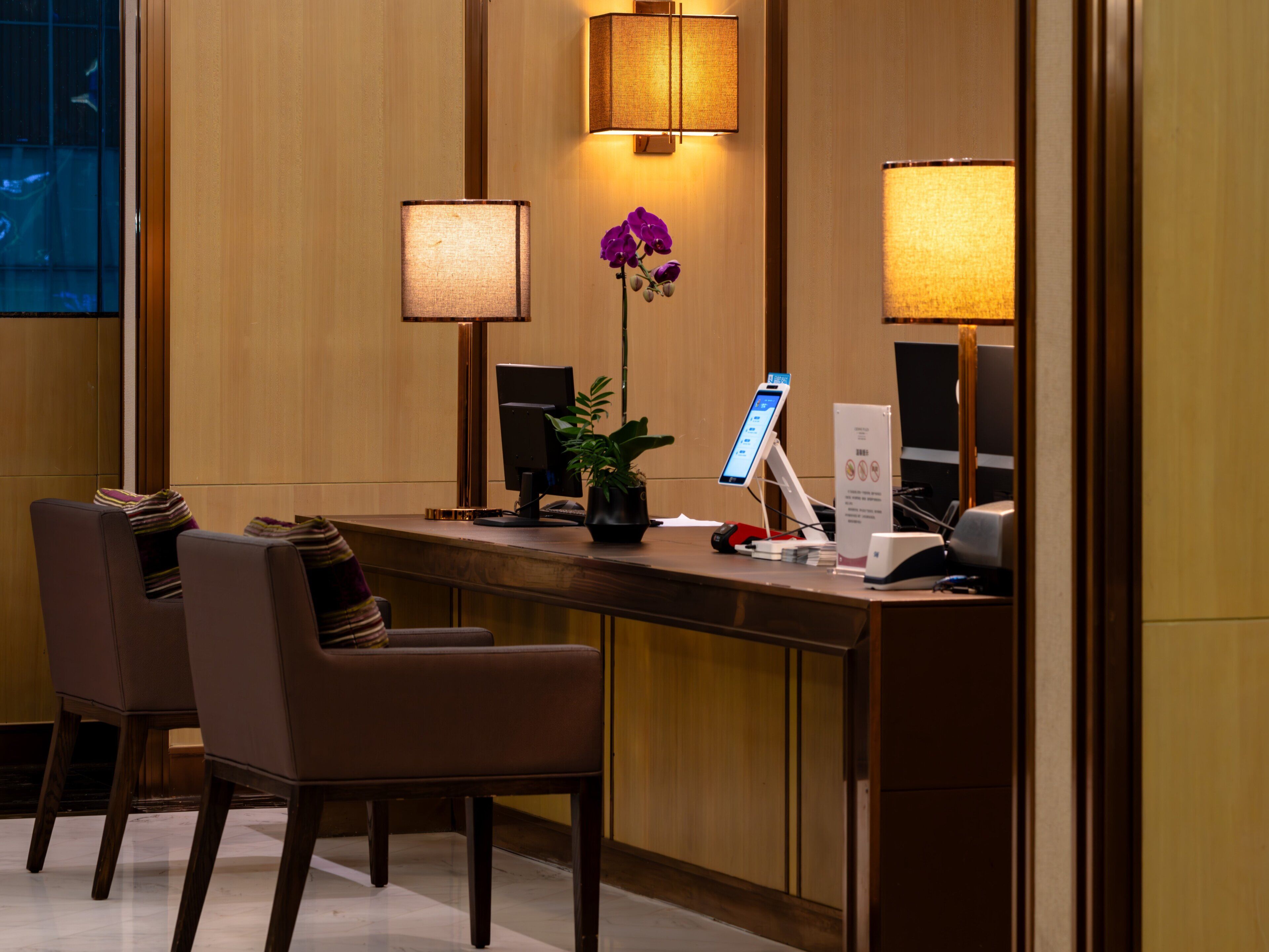 Un comptoir d’accueil d’hôtel avec deux chaises, un ordinateur, un téléphone et une plante en pot.