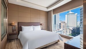 Een hotelkamer met een groot bed, een nachtkastje, een lamp, een spiegel en uitzicht op de stad.