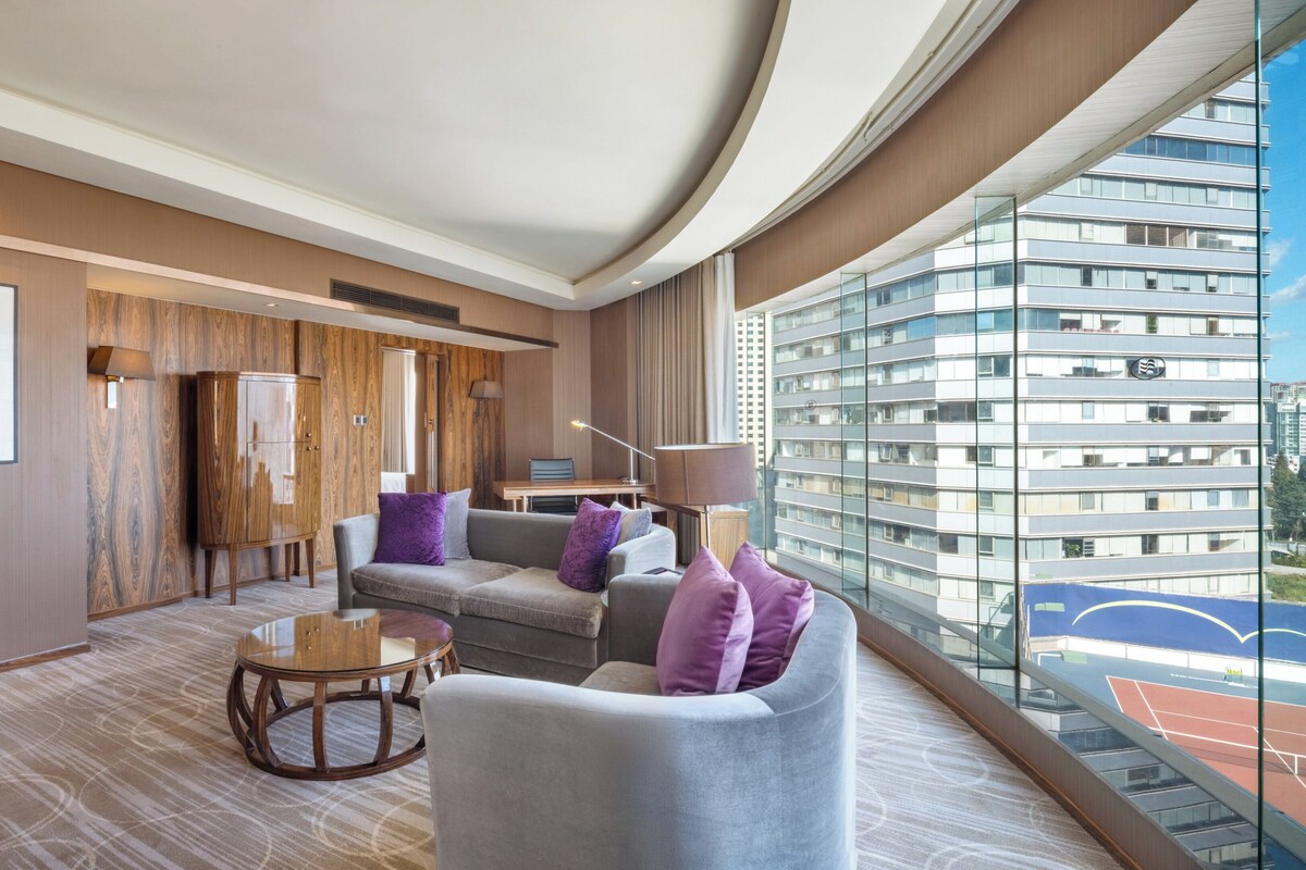Une chambre d’hôtel moderne avec une grande fenêtre, un canapé, une petite table ronde et un meuble.