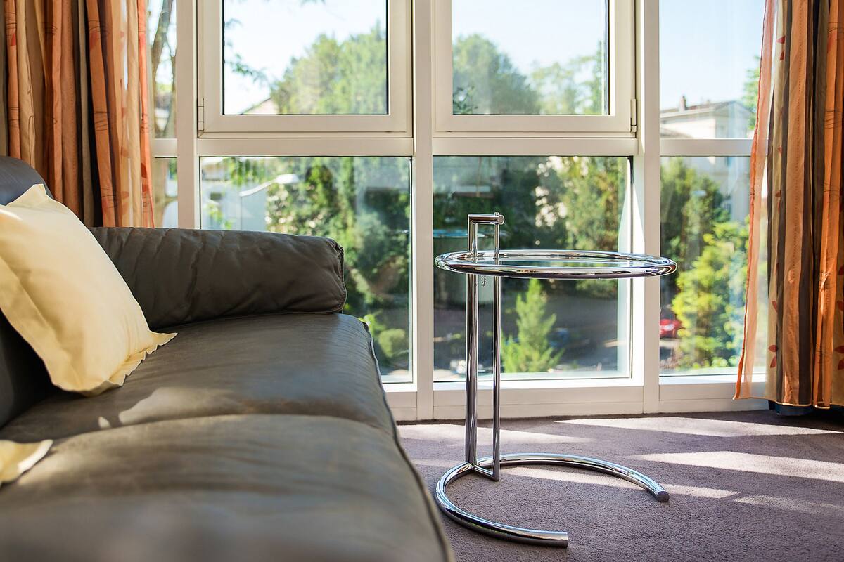 Ein modernes Wohnzimmer mit Ledersofa, Glastisch und Blick auf Grün durch große Fenster.