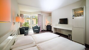 Ein Hotelzimmer mit Bett, Schreibtisch, Stuhl, Fernseher und einem Fenster mit Vorhängen.
