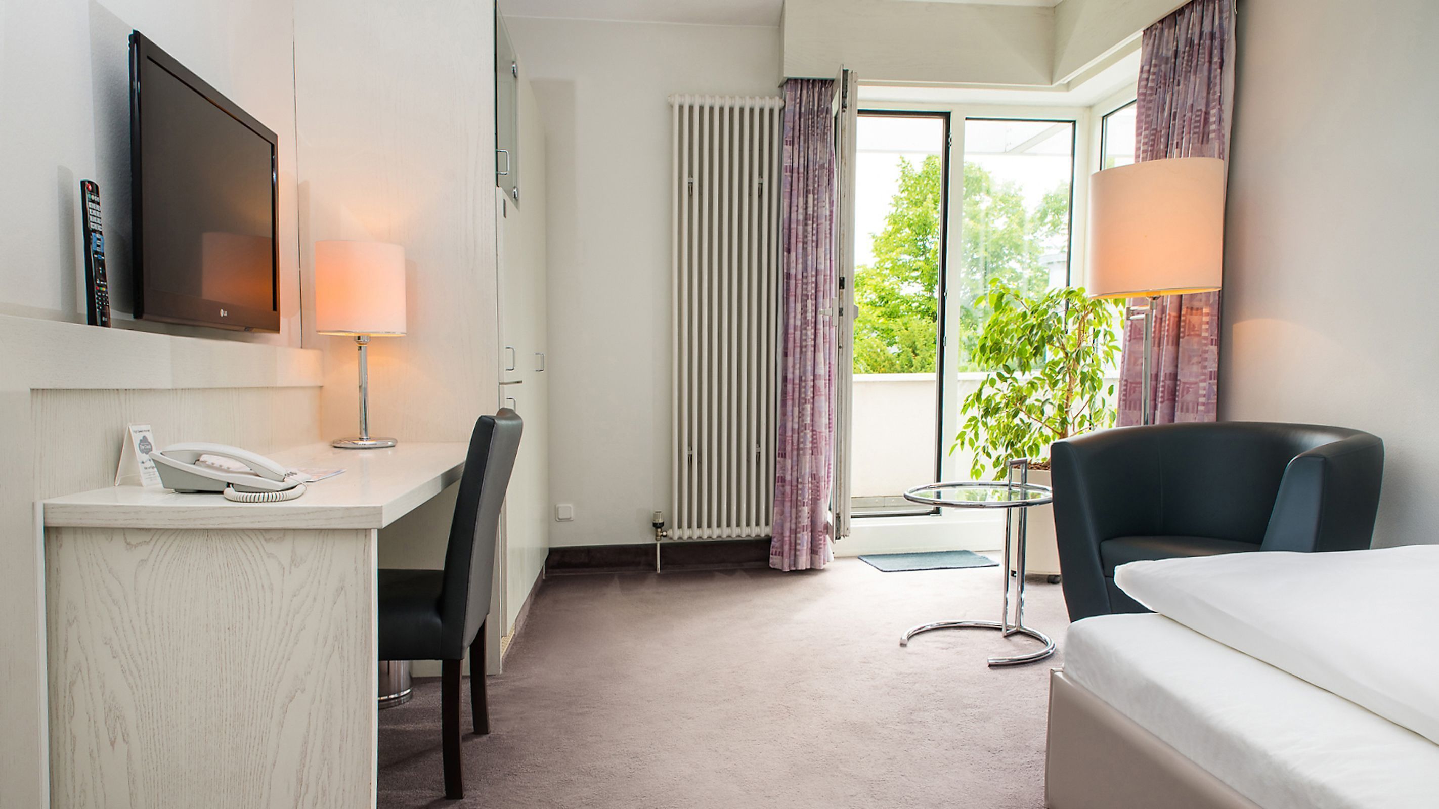 Habitación de hotel con escritorio, silla, cama, televisión y ventana con cortinas.
