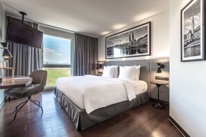 A hotel room with a large bed, a desk, a chair, and a TV. - Radisson Hotel Zurich Airport (Ruemlang)