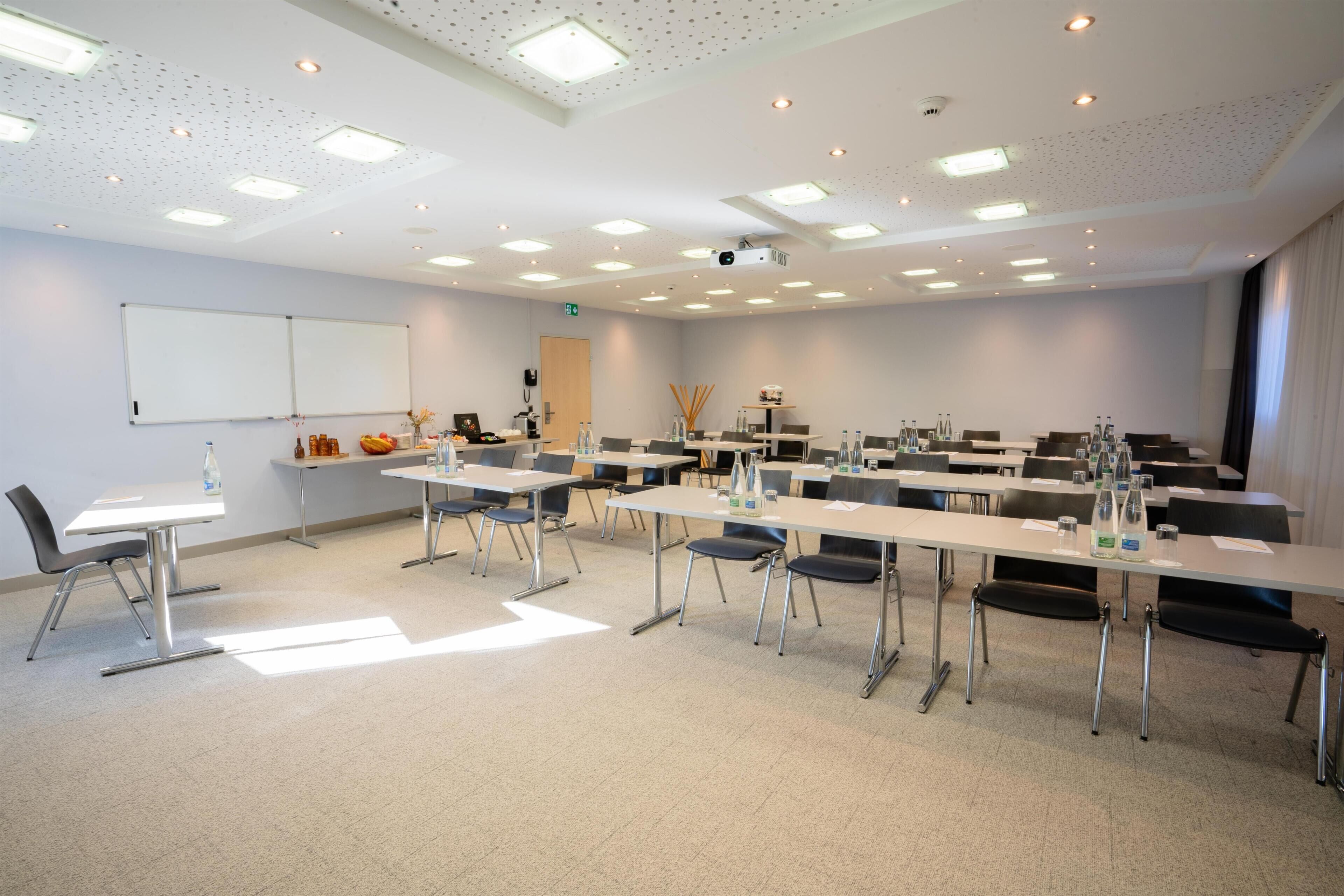 Un salón de conferencias con mesas, sillas, una pizarra y un proyector.