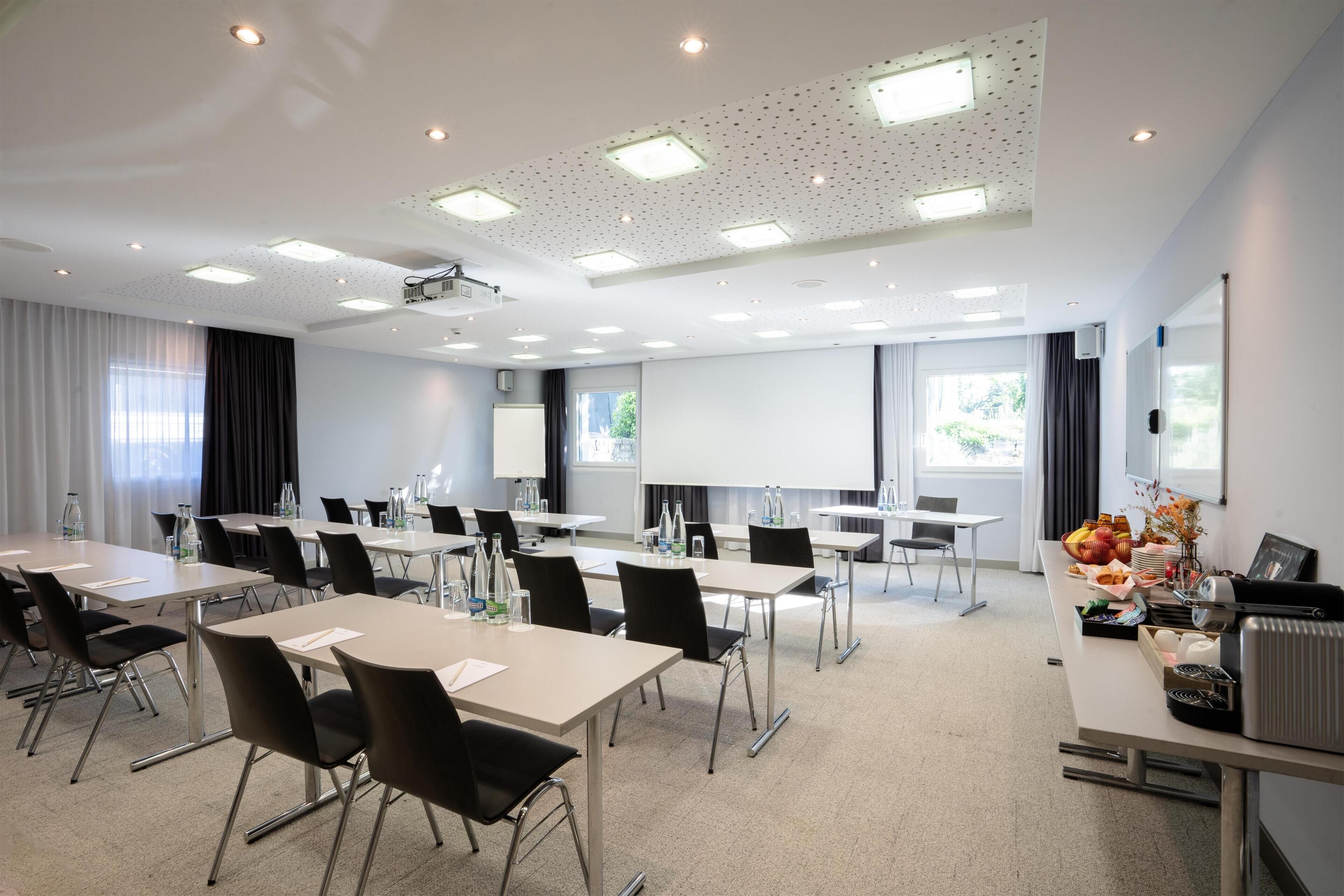 A conference room with tables, chairs, a projector, and a screen.