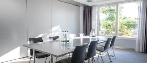 Un salón de conferencias con una larga mesa, cuatro sillas y un amplio ventanal con cortinas.
