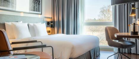 A hotel room with a bed, a desk, a chair, and a large window with curtains.